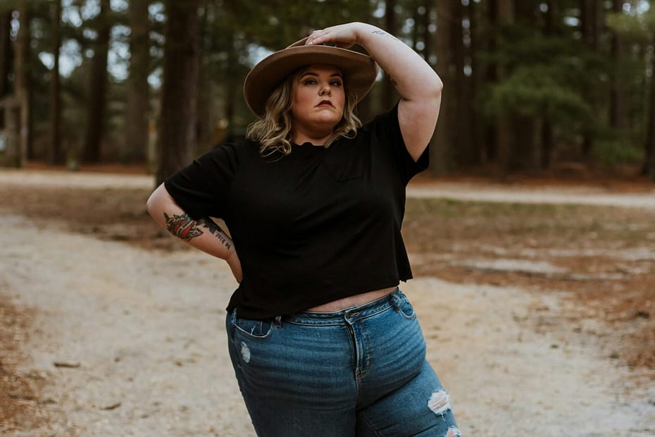 woman in black t-shirt and blue denim jeans standing on dirt road during daytime